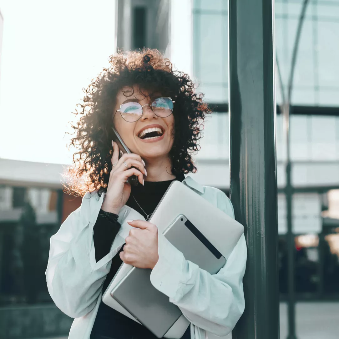 Person mit Smartphone am Ohr und einem Tblet in der Hand steht vor einem Gebäude