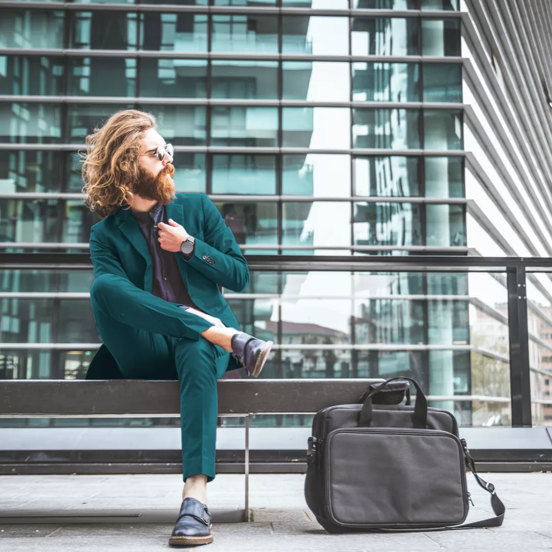 Persoon mit Bart und langen Haaren sitzt bei Wind auf einer Bank