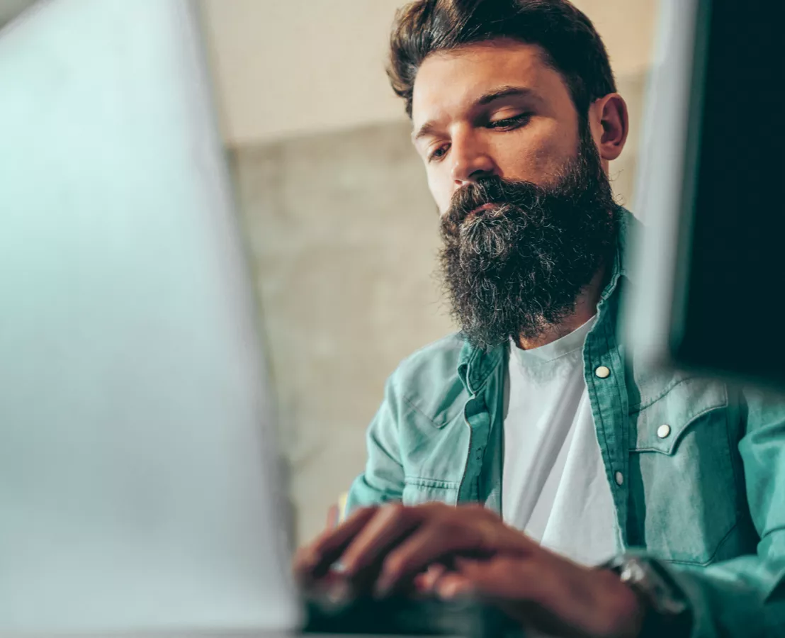 Person mit kurzen Haaren und langem Bart sich vor einem Notebook